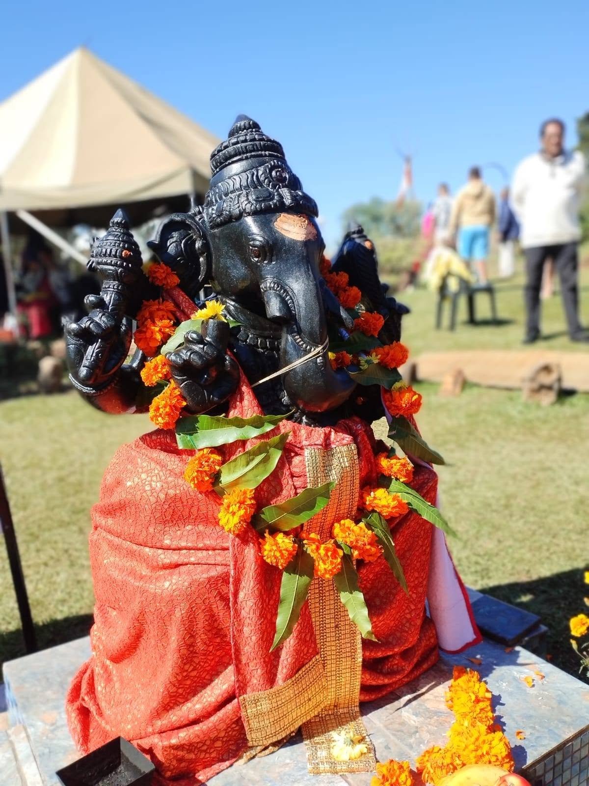 Black stone Ganesh murti draped in red and gold cloth with marigold garlands at Shiva Kshetra